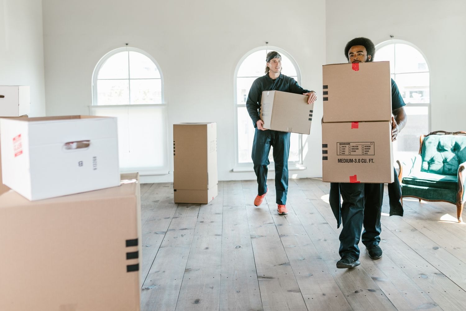 Two helpers carrying boxes through a bright room
